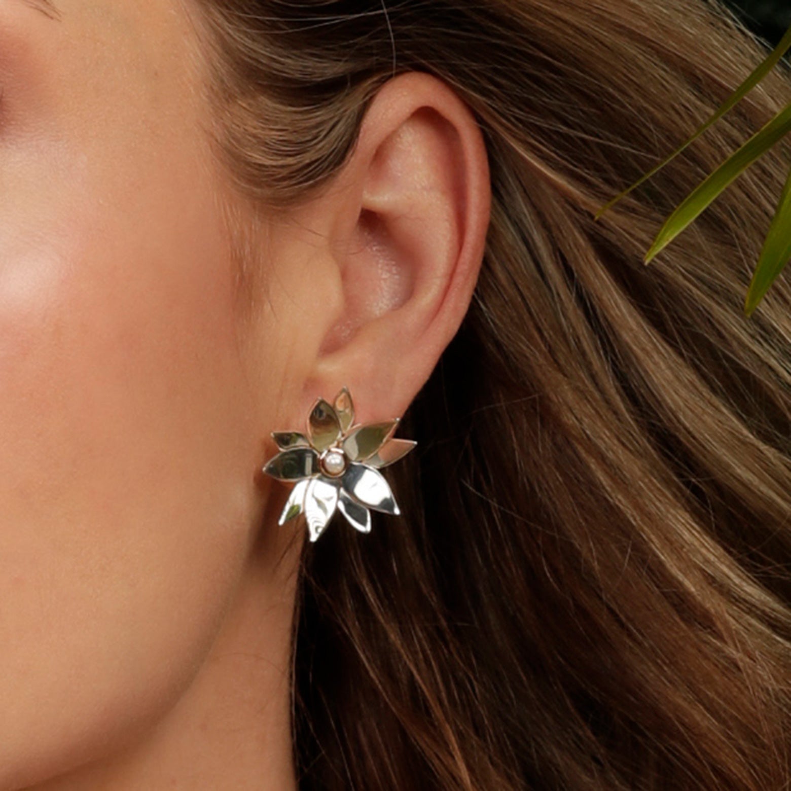 A close up of an ear wearing the Kelly Woodcroft daintree bloom earrings. They are silver and form flower shapes with a rose-gold set pearl in the centre.