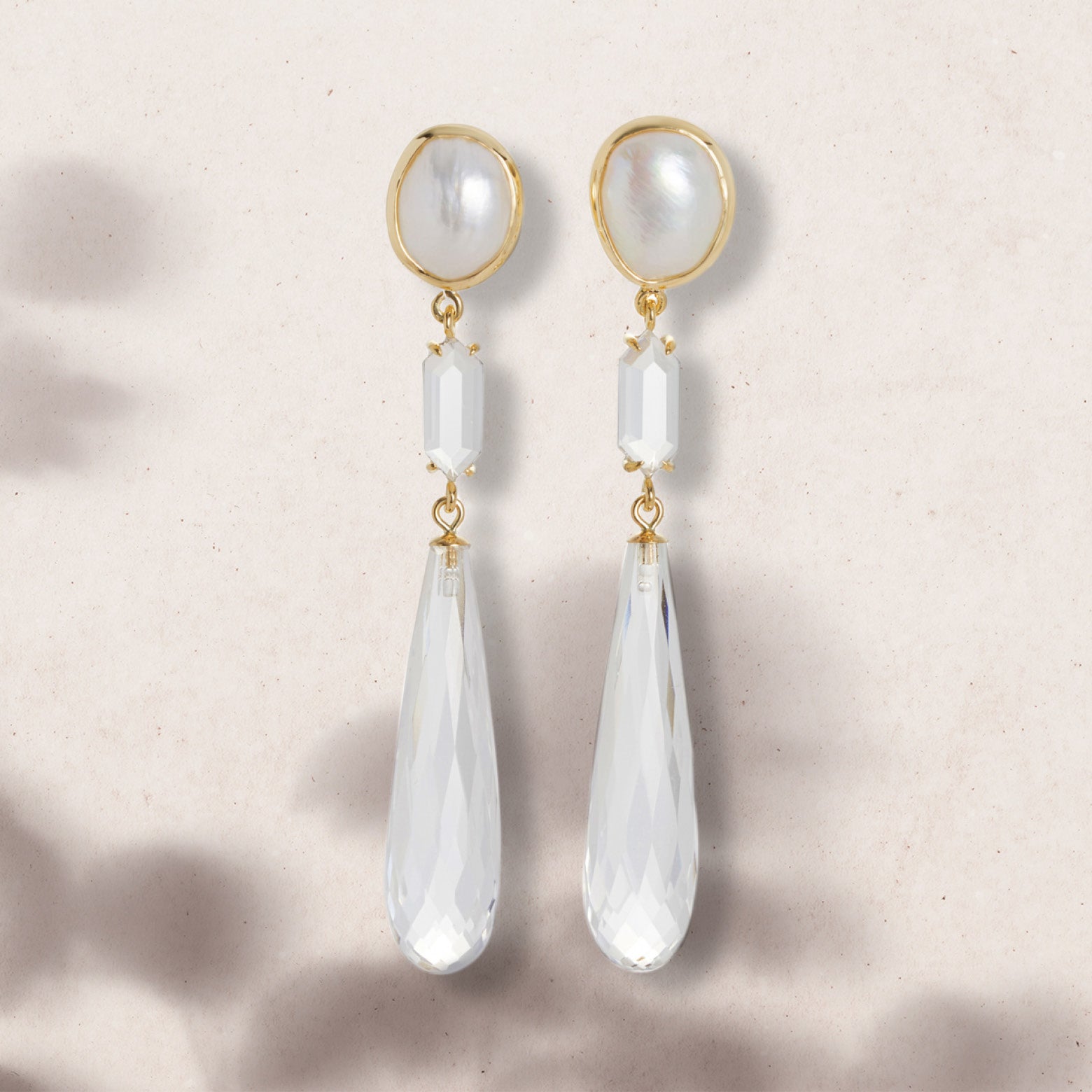Flat lay of drop earrings with pearl and faceted clear quartz set in yellow gold
