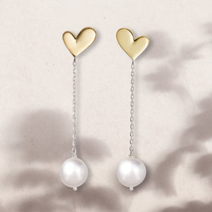 Flat lay of gold heart earrings with chain detail and pearl