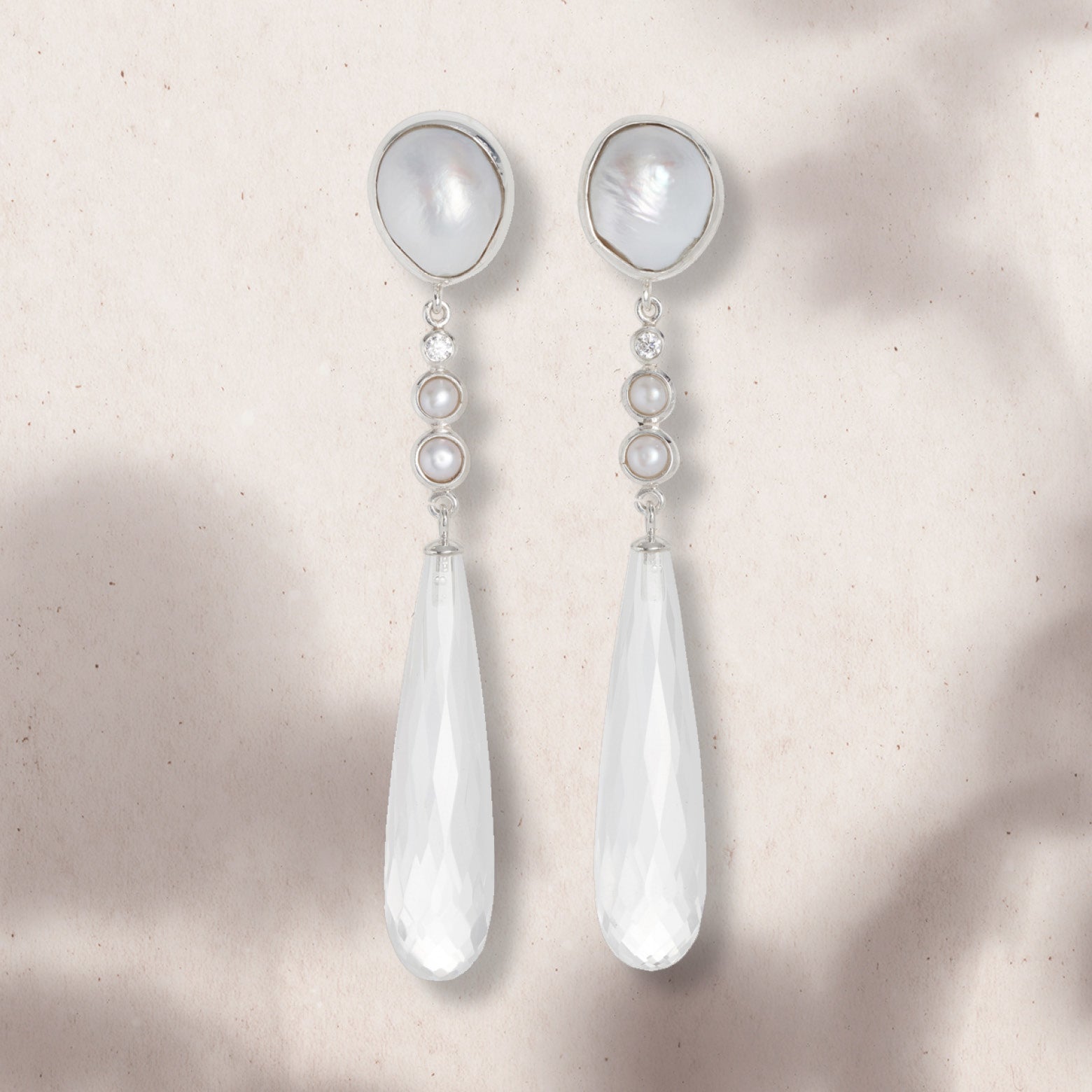 Flat lay of drop earrings with three pearls and a faceted quartz drop set in silver