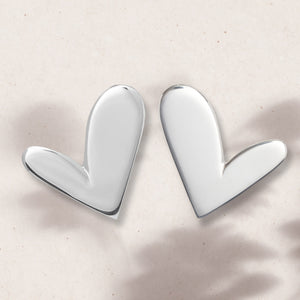 Flat lay of mini asymmetric silver heart earrings
